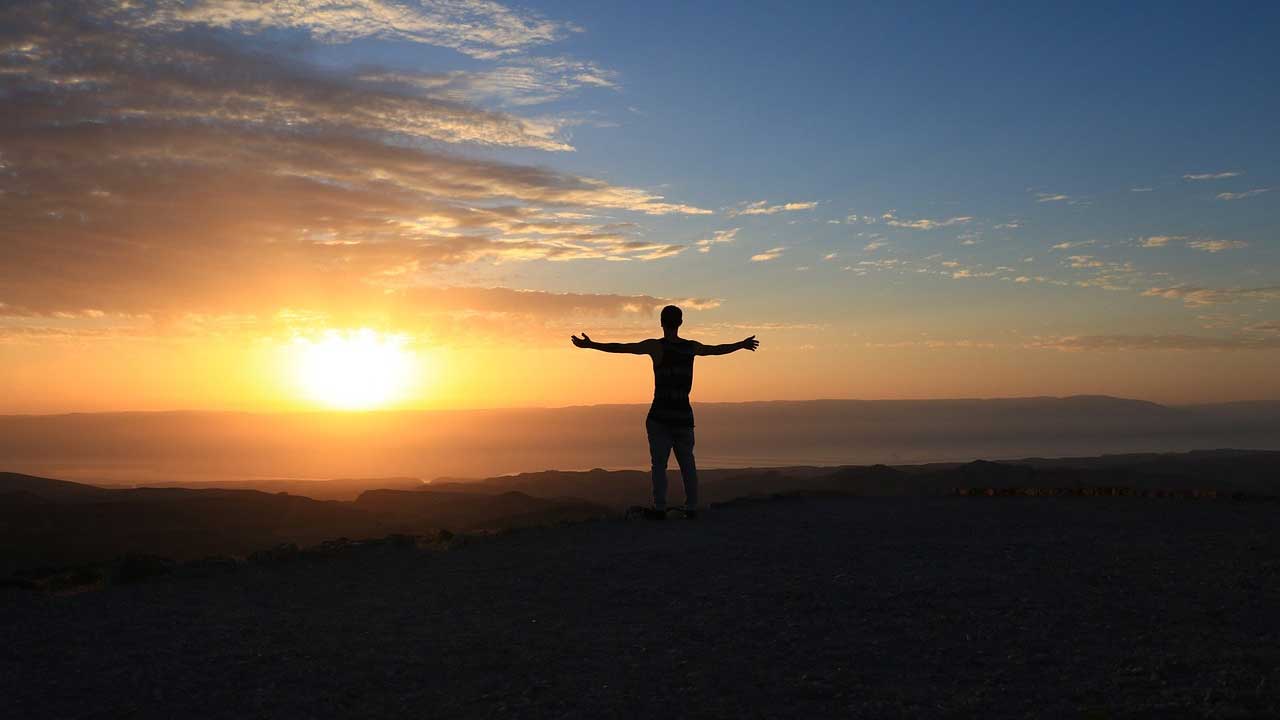 person-looking-at-sunset-with-arms-open